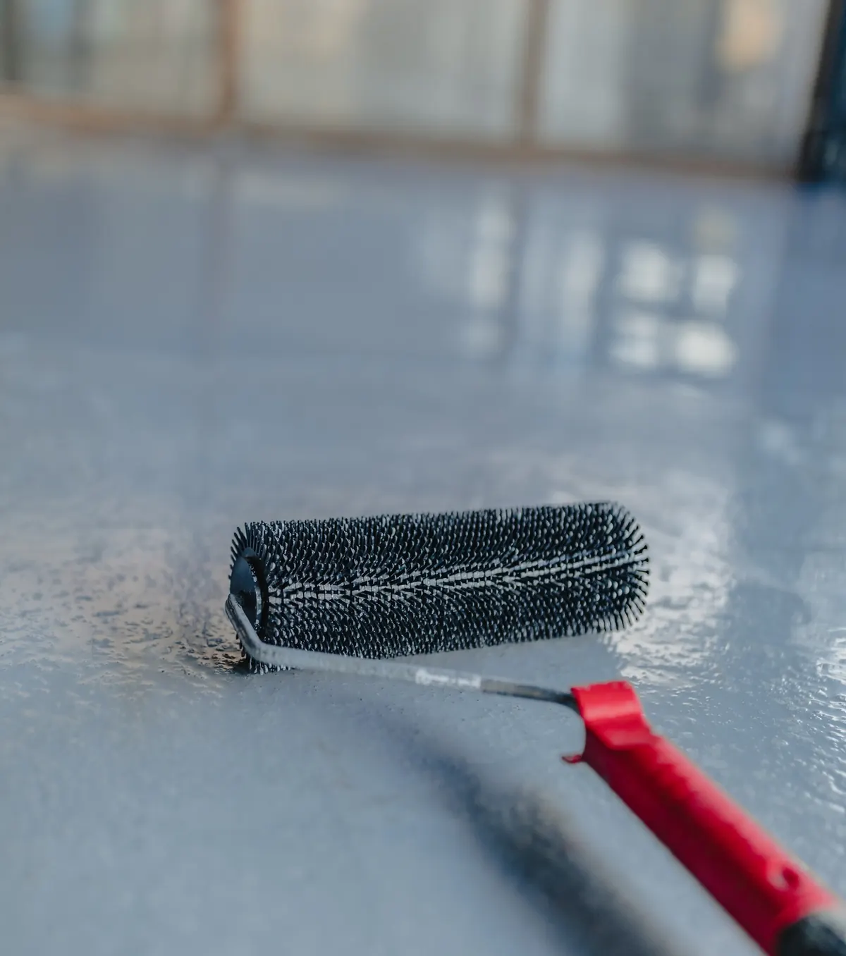 Close-up of an epoxy base coat being spread with a squeegee over diamond-ground concrete