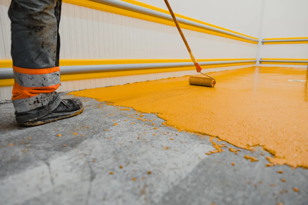 Installer spreading a self-leveling epoxy coat with a notched squeegee over prepared concrete